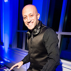 A man in black shirt and tie smiling.