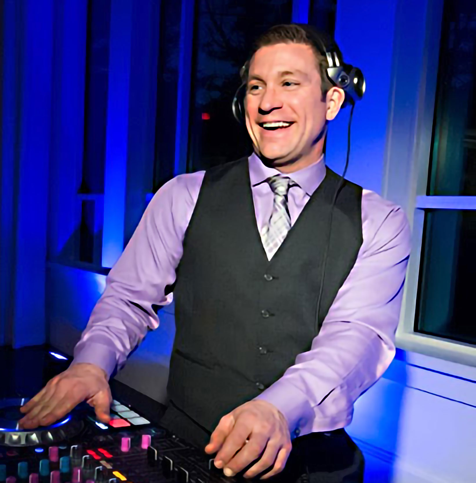 A man in purple shirt and vest holding a dj controller.