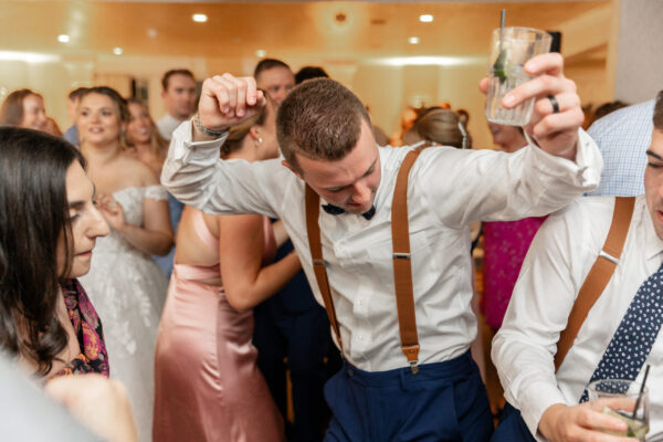 A man in suspenders and bow tie dancing with other people.