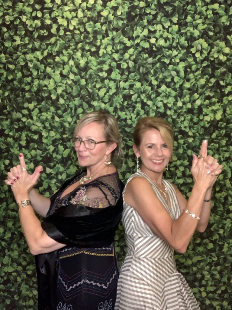 Two women posing for a picture in front of a wall. Two women posing for a picture in front of a wall.