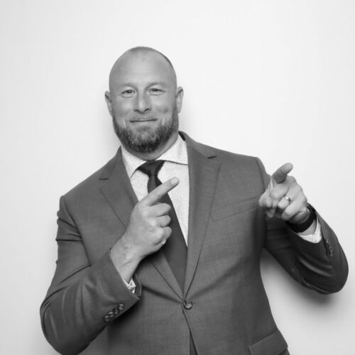 A man in suit and tie pointing to his chest.