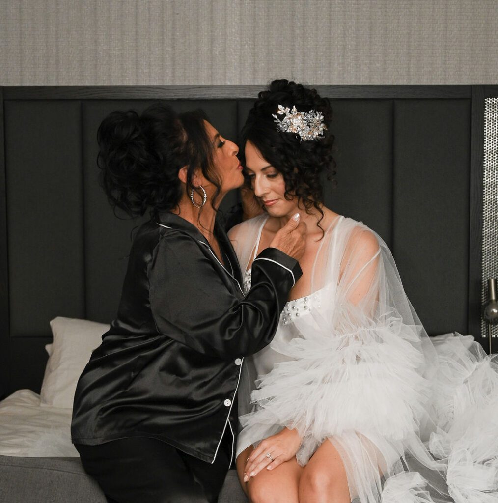 Two women sharing a tender moment in elegant attire, one in black satin and the other in a white bridal robe. Two women sharing a tender moment in elegant attire, one in black satin and the other in a white bridal robe.