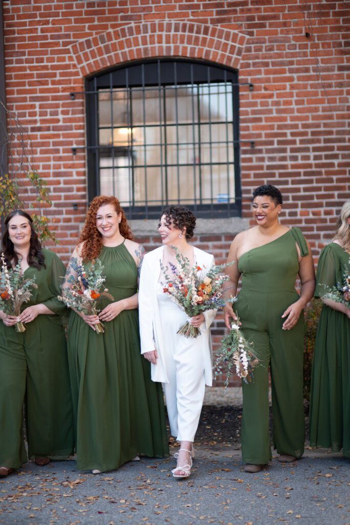 A bridal party with bridesmaids in green dresses and a bride in a white suit holding flowers. A bridal party with bridesmaids in green dresses and a bride in a white suit holding flowers.