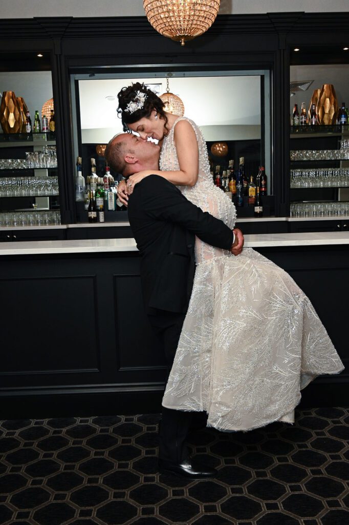 Groom lifting bride in front of a bar, sharing a joyful moment. Groom lifting bride in front of a bar, sharing a joyful moment.