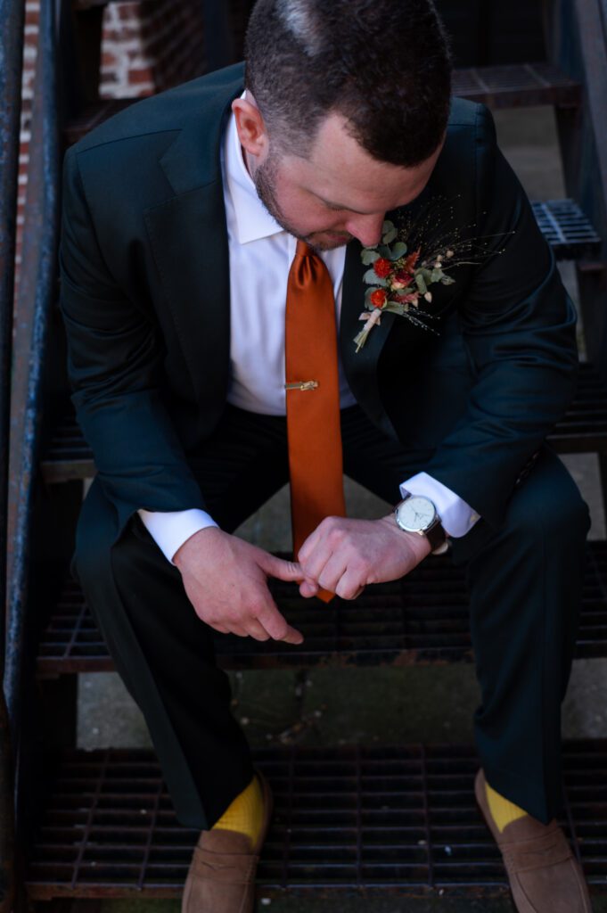 Man in a suit checking his watch with an orange tie and boutonniere. Man in a suit checking his watch with an orange tie and boutonniere.
