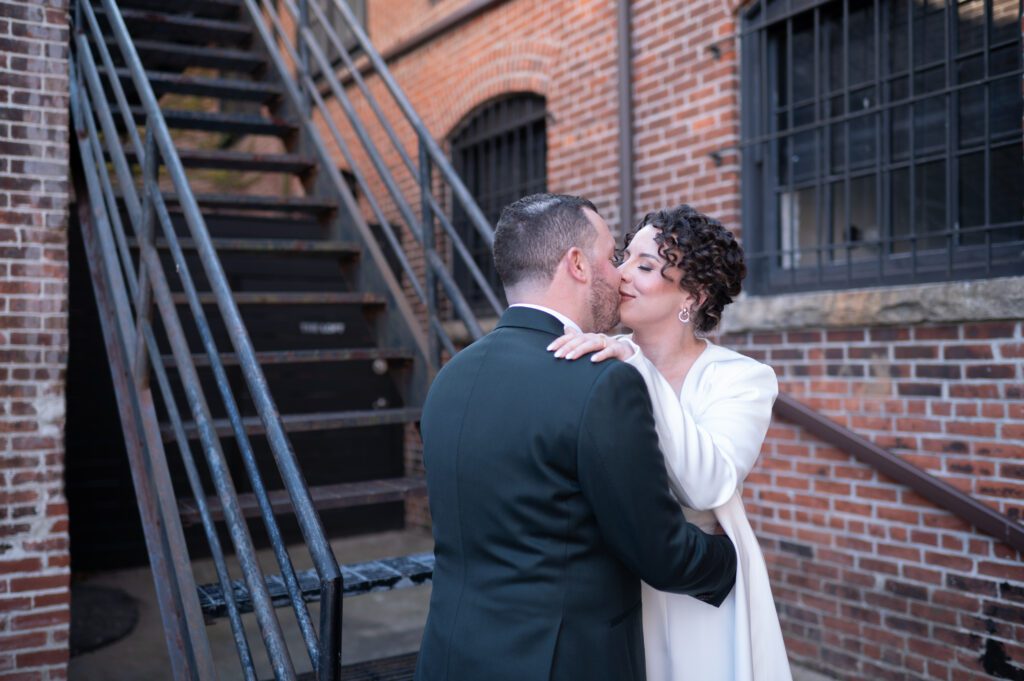 A couple shares a romantic kiss near a brick building and metal staircase. A couple shares a romantic kiss near a brick building and metal staircase.