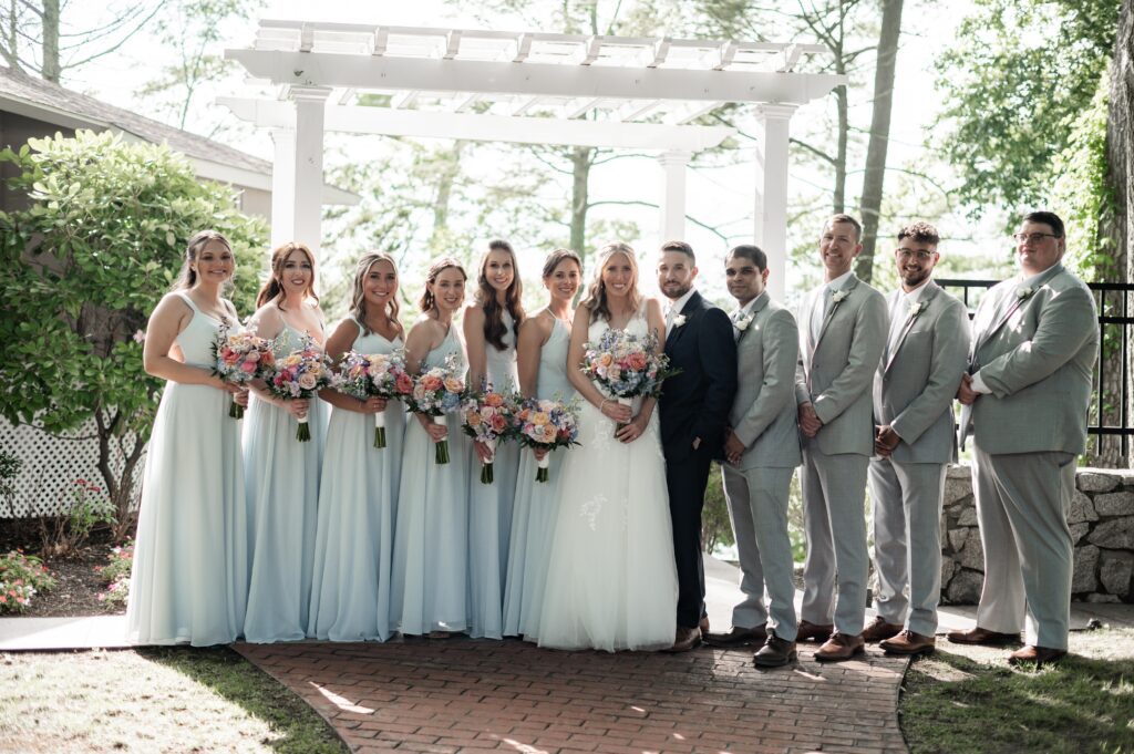 Bride and groom with bridal party in light attire under pergola. Bride and groom with bridal party in light attire under pergola.