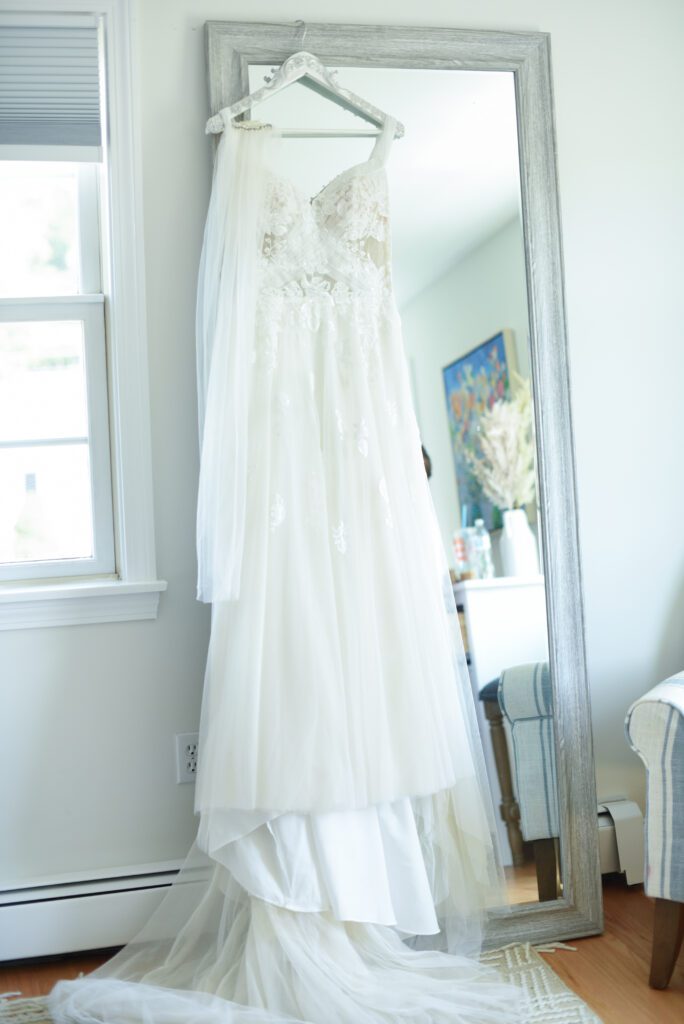 Elegant white wedding dress hanging in a bright room near a window. Elegant white wedding dress hanging in a bright room near a window.