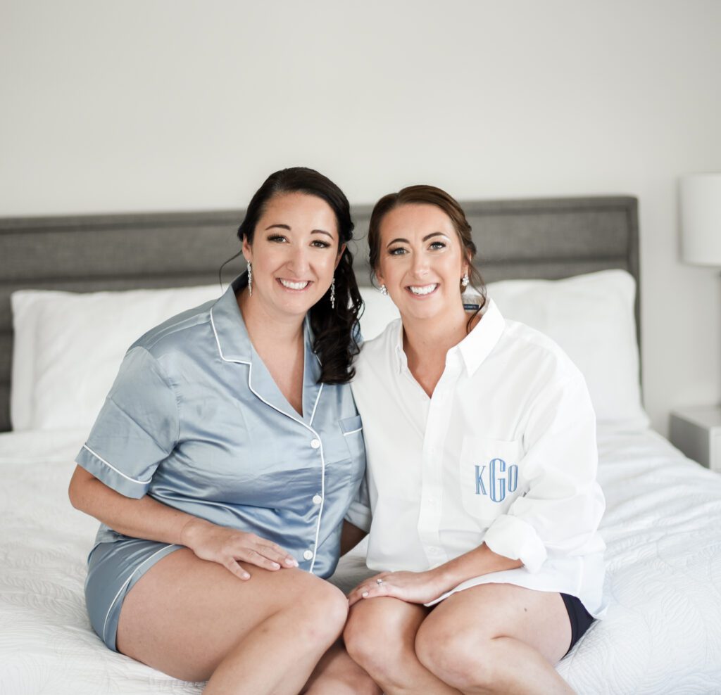 Two women in satin pajamas sitting on a bed, smiling. Two women in satin pajamas sitting on a bed, smiling.