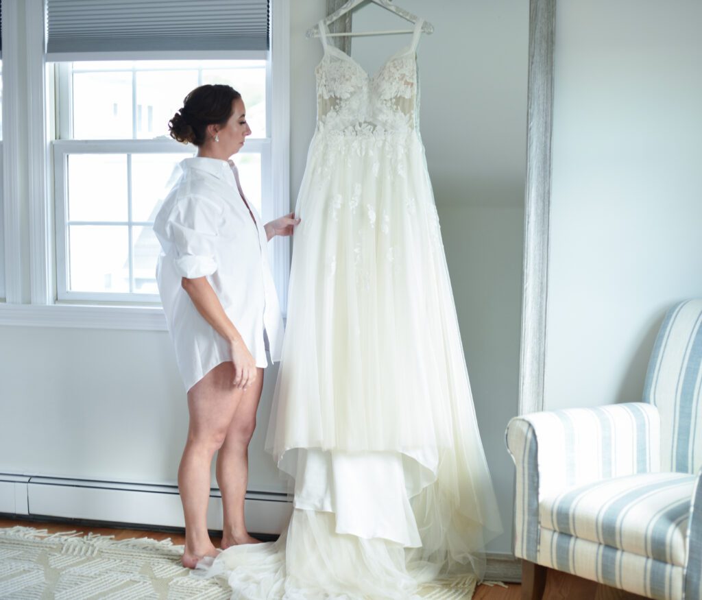 Woman in a robe admiring a hanging wedding dress in a bright room. Woman in a robe admiring a hanging wedding dress in a bright room.