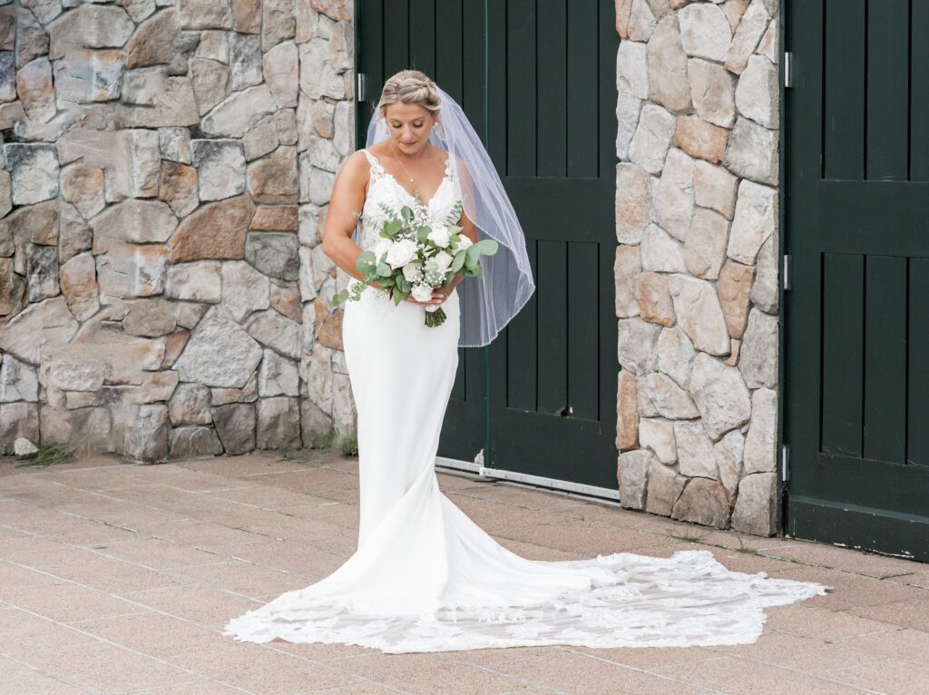 Bride in elegant white gown holding bouquet, standing before green doors and stone wall. Bride in elegant white gown holding bouquet, standing before green doors and stone wall.