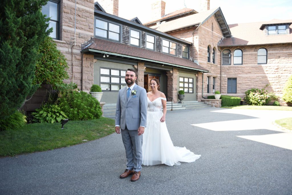 Bride and groom standing in front of a large house on their wedding day. Bride and groom standing in front of a large house on their wedding day.