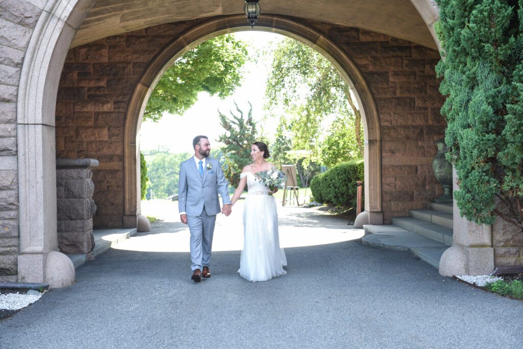 Newlywed couple walking hand in hand under an archway on their wedding day. Newlywed couple walking hand in hand under an archway on their wedding day.