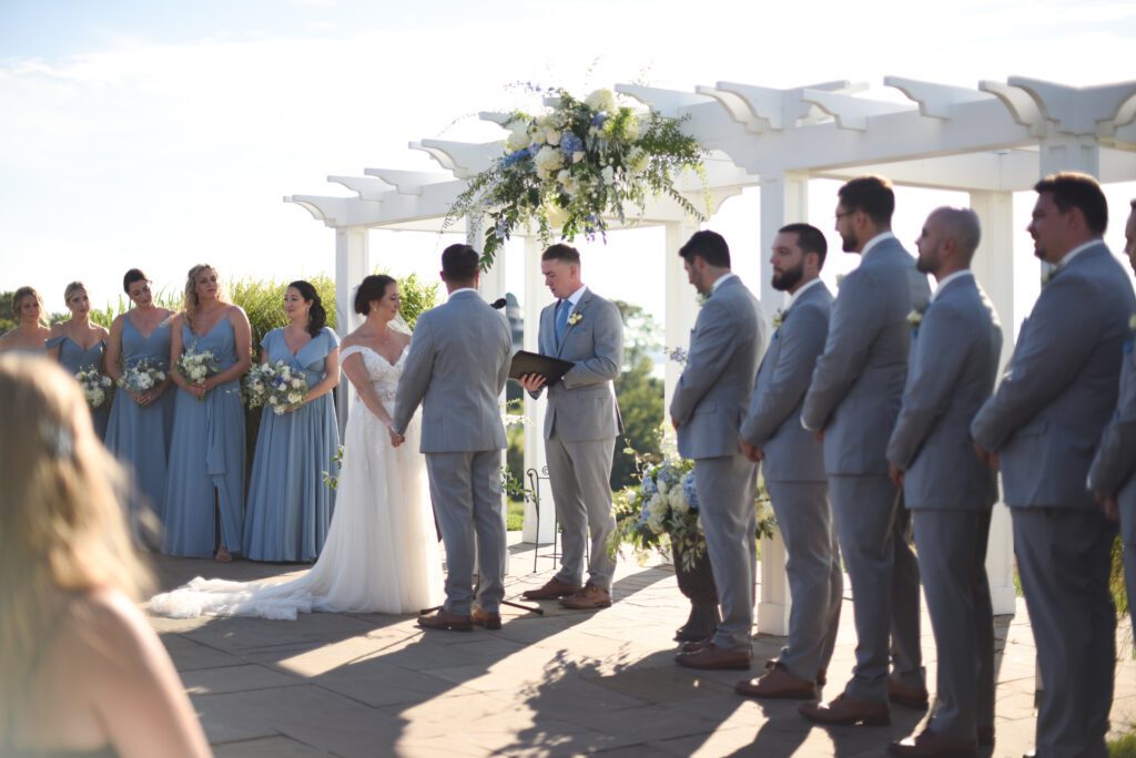 Couple exchanging vows at an outdoor wedding with bridal party beside them. Couple exchanging vows at an outdoor wedding with bridal party beside them.
