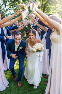 Bride and groom smiling under a floral arch made by friends.
