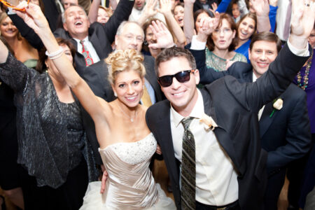 A bride and groom posing for the camera with their arms raised.