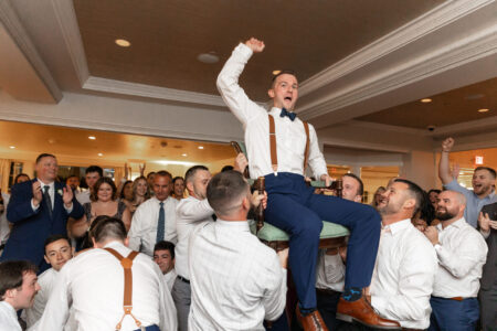A man in white shirt and blue pants jumping on chair.