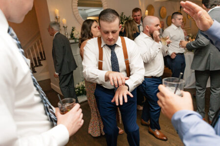 A man in suspenders and tie standing next to other people.
