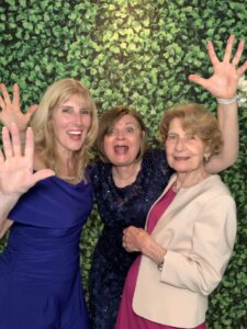 Three women posing for a picture in front of a green wall.