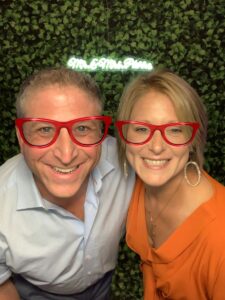 A man and woman posing for the camera with red glasses on.