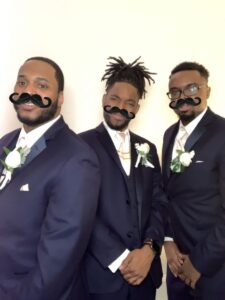 Three men in suits and ties with fake mustaches on their heads.