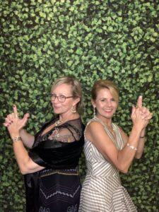 Two women posing for a picture in front of a wall.