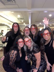 A group of women wearing red glasses and smiling.