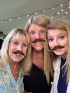 Three women with fake mustaches on their faces.