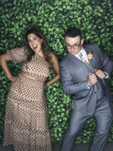 A man and woman posing for a picture in front of a wall covered with green leaves.