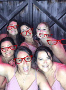 A group of women wearing red glasses and smiling.