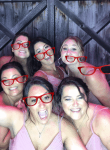A group of women wearing red glasses and smiling.