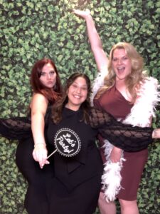 Three women posing for a photo in front of a green wall.