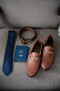 Men's accessories including loafers, a belt, tie, and a book on style.