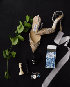 Elegant woven high-heeled shoes with a chess piece and perfume on a dark background.
