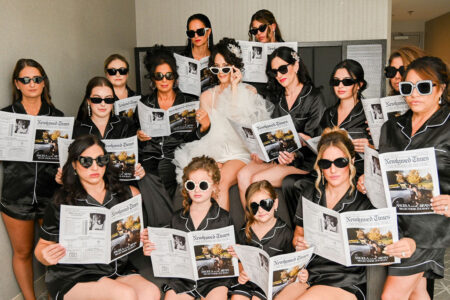 Group of women in matching robes and sunglasses reading newspapers indoors.