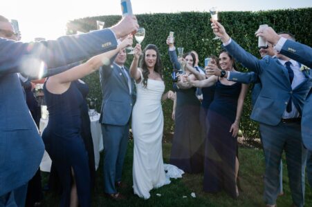 Bride and groom toast with friends in an outdoor celebration.