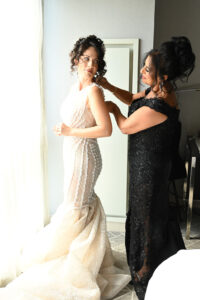 A bride getting help with her wedding dress from a woman in a black gown.