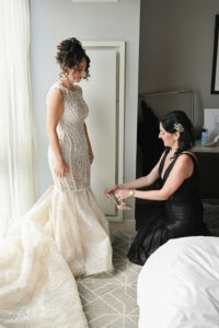 Bride in elegant gown being helped by woman in black dress.