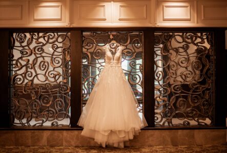 Elegant wedding dress hanging in a warmly lit room with ornate ironwork doors.