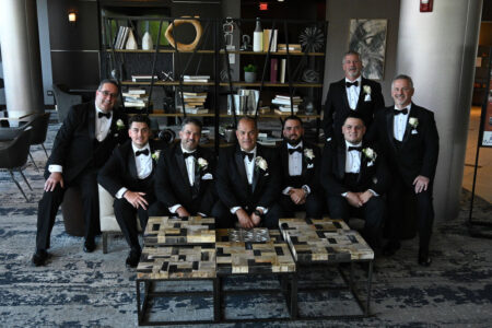 A group of men in tuxedos posing in a sophisticated room with bookshelves.