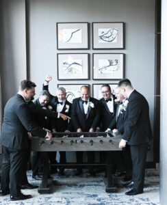 Men in tuxedos playing foosball in a stylish room.