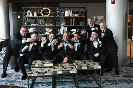 A group of men in tuxedos posing with drinks in a stylish room.