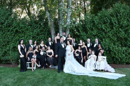 Large wedding party posing outdoors with bride and groom in center.