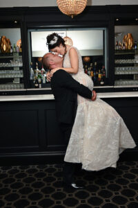 Groom lifting bride in front of a bar, sharing a joyful moment.