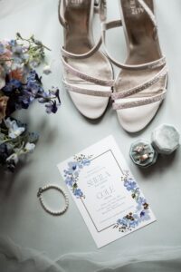 Elegant wedding invitation with floral design, rings, and bridal shoes.