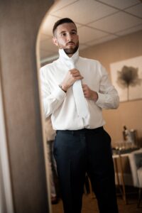 Man buttoning up a white dress shirt in a softly lit room.