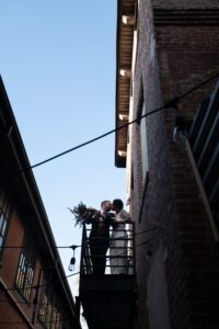 A couple embracing on a balcony between two buildings under a clear sky.