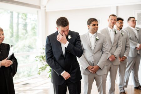 Groom wiping tears during emotional moment at wedding.