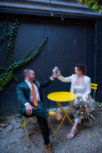 Newlyweds toast at a vibrant yellow table in an outdoor setting.