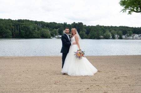 Bride and groom posing on a sandy beach by the lake.